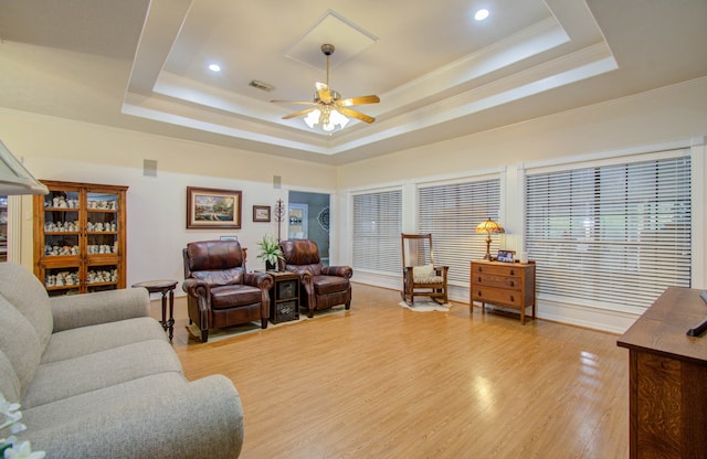 living room with ornamental molding, light hardwood / wood-style floors, a tray ceiling, and ceiling fan