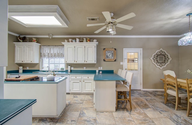 kitchen with ceiling fan, a kitchen island, crown molding, and white cabinetry