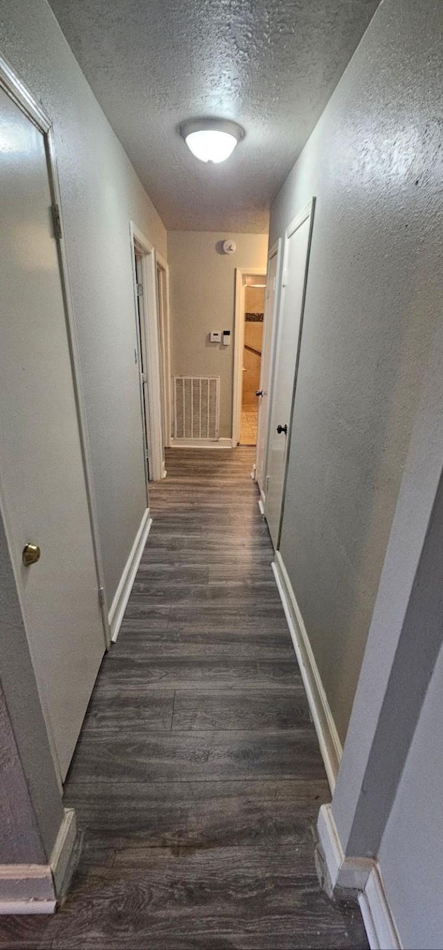 hall with a textured ceiling and dark hardwood / wood-style floors