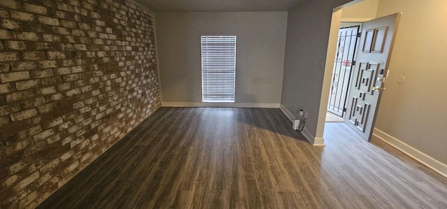 spare room featuring dark hardwood / wood-style flooring and brick wall