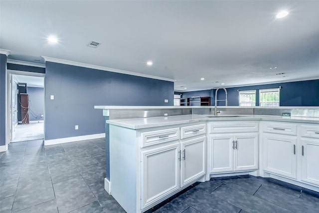 kitchen with dark tile patterned floors, white cabinets, crown molding, and sink