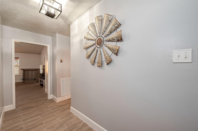 corridor with light hardwood / wood-style floors and a textured ceiling