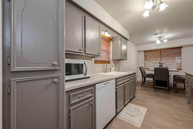 kitchen featuring sink, a notable chandelier, light hardwood / wood-style floors, white appliances, and gray cabinets