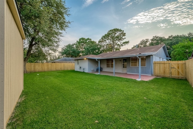 back house at dusk featuring a lawn and a patio