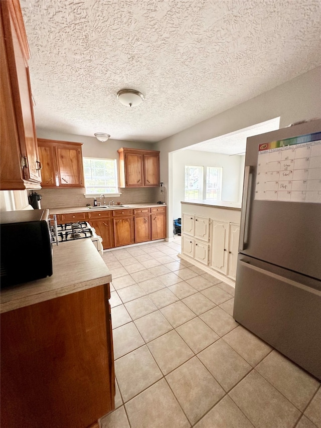 kitchen featuring range, sink, a textured ceiling, stainless steel fridge, and light tile patterned flooring