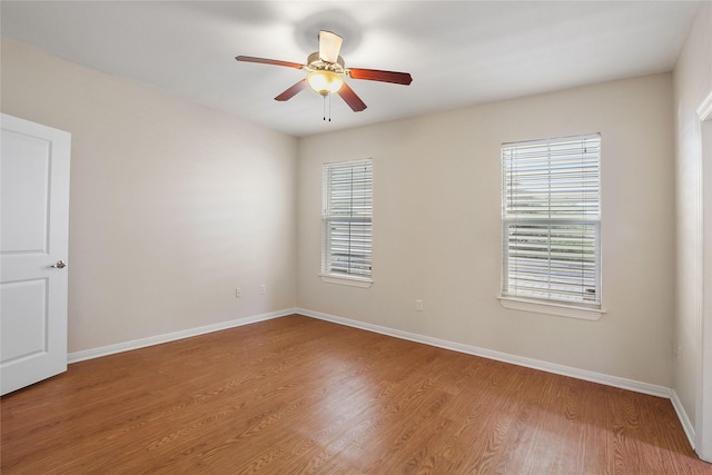 empty room with wood finished floors, a ceiling fan, and baseboards