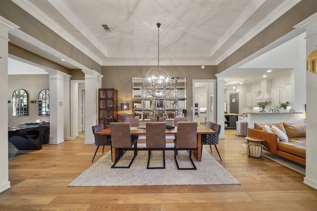 dining space with light wood-type flooring, decorative columns, a tray ceiling, and an inviting chandelier