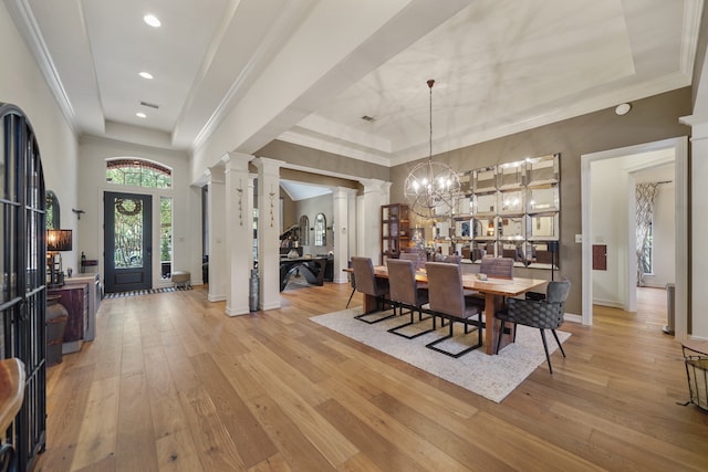 dining area featuring an inviting chandelier, decorative columns, light hardwood / wood-style flooring, and a tray ceiling