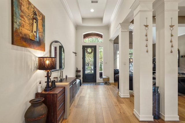 entryway with light hardwood / wood-style floors, ornamental molding, decorative columns, a tray ceiling, and a towering ceiling