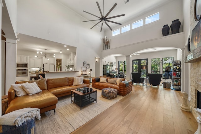 living area featuring arched walkways, a stone fireplace, ceiling fan with notable chandelier, light wood-style floors, and ornate columns