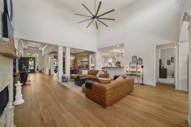 living room with ceiling fan, light hardwood / wood-style flooring, ornate columns, a towering ceiling, and a fireplace