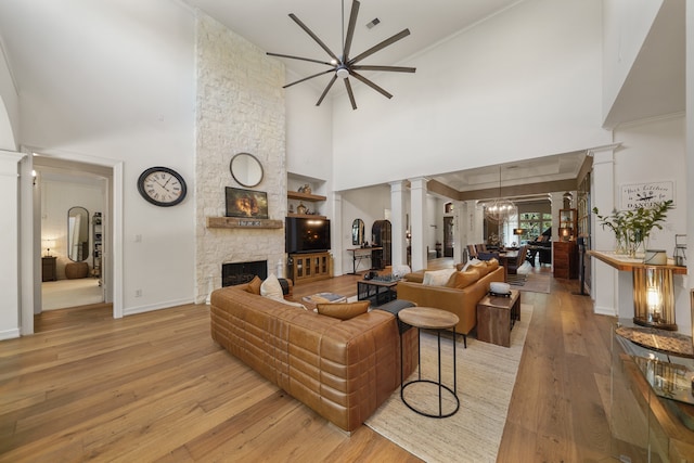 living room featuring light hardwood / wood-style flooring, ornate columns, a stone fireplace, and a towering ceiling