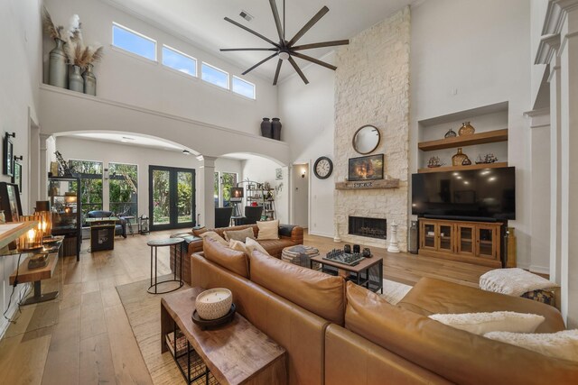 living room featuring a fireplace, light hardwood / wood-style flooring, a towering ceiling, ceiling fan, and decorative columns