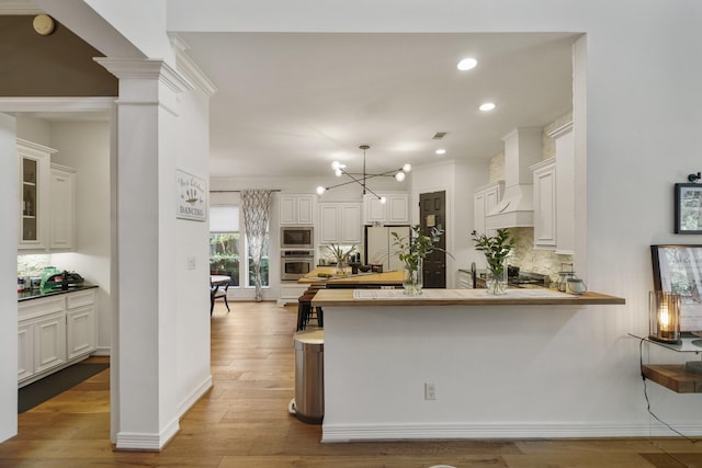 kitchen featuring appliances with stainless steel finishes, light countertops, premium range hood, and white cabinetry