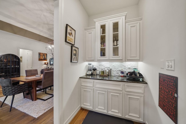 bar featuring light wood finished floors, baseboards, a chandelier, bar area, and backsplash