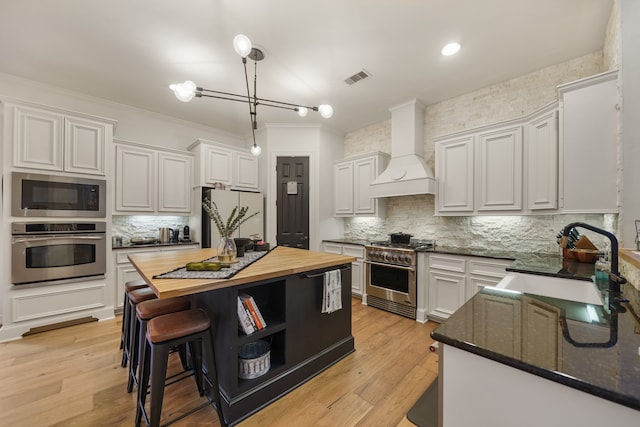 kitchen with custom range hood, stainless steel appliances, white cabinetry, sink, and wooden counters