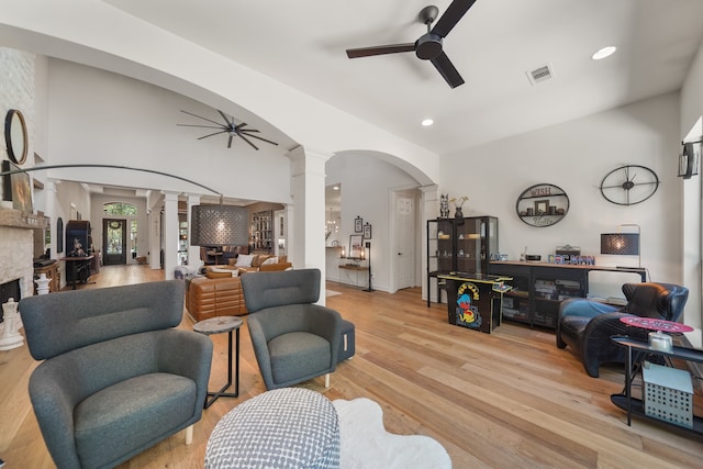 living room with a fireplace, light hardwood / wood-style flooring, ceiling fan, and ornate columns