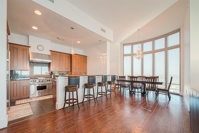 kitchen with wall chimney range hood, pendant lighting, dark wood-type flooring, a kitchen bar, and stainless steel range