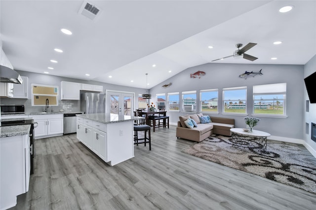 kitchen featuring a kitchen island, stainless steel appliances, vaulted ceiling, light wood-type flooring, and white cabinetry