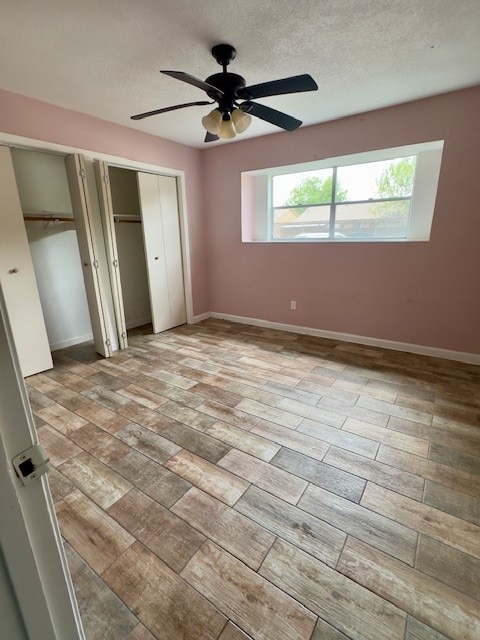 unfurnished bedroom with multiple windows, ceiling fan, a textured ceiling, and multiple closets