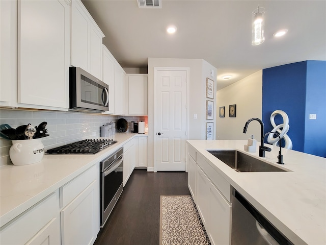 kitchen with sink, appliances with stainless steel finishes, dark wood-type flooring, tasteful backsplash, and white cabinets