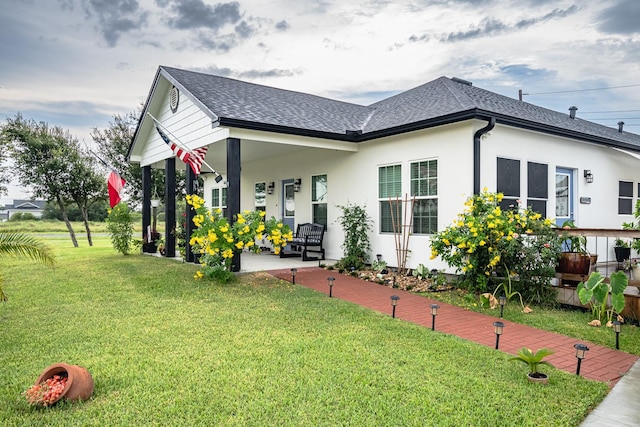 view of front of property with stucco siding, a shingled roof, and a front yard