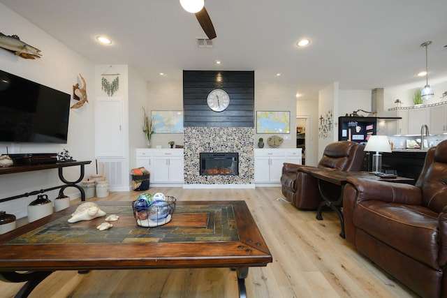 living room with light wood-style flooring, a tiled fireplace, visible vents, and recessed lighting