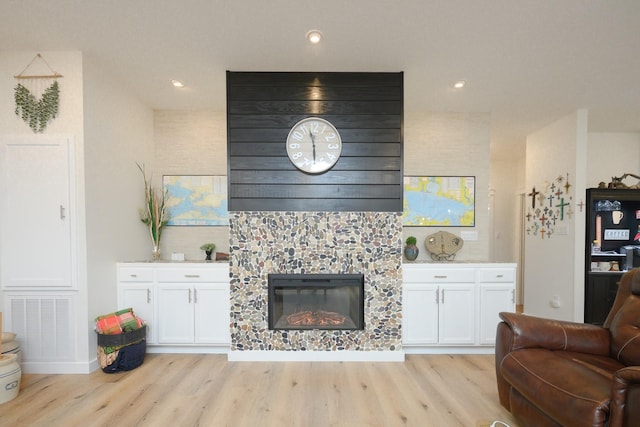 living area featuring light wood-type flooring, recessed lighting, visible vents, and a stone fireplace