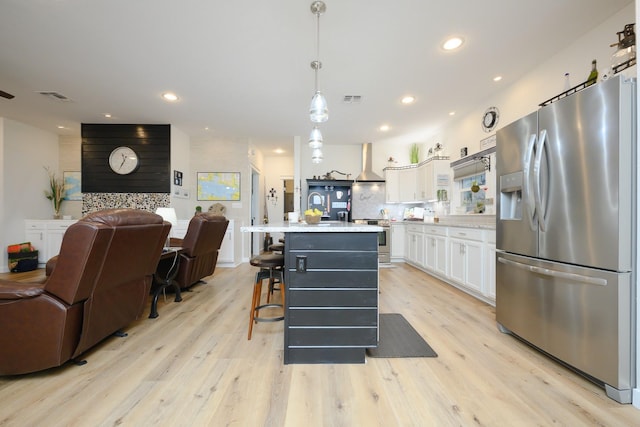 kitchen with stainless steel appliances, light countertops, open floor plan, white cabinets, and wall chimney range hood