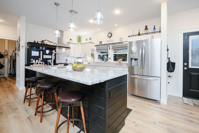 kitchen featuring light wood finished floors, stainless steel fridge, decorative backsplash, white cabinets, and a sink