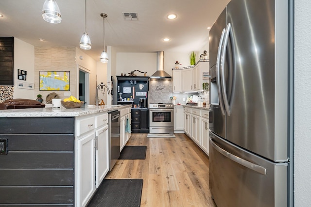 kitchen featuring decorative backsplash, appliances with stainless steel finishes, white cabinets, a sink, and wall chimney exhaust hood