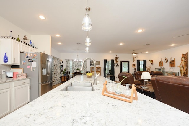 kitchen with white cabinets, stainless steel fridge, hanging light fixtures, and a sink