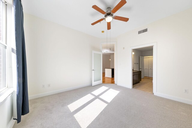 unfurnished bedroom with ceiling fan, connected bathroom, multiple windows, and light carpet