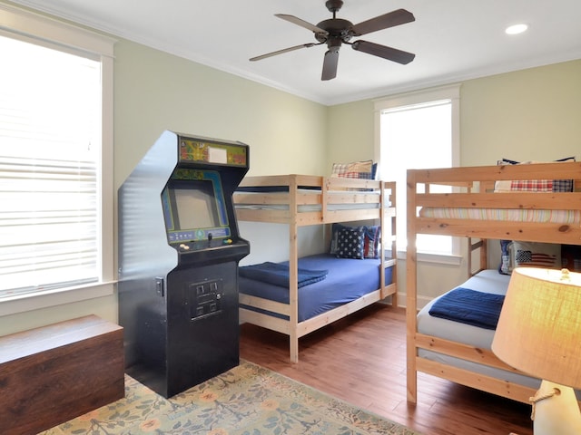 bedroom featuring ceiling fan, ornamental molding, multiple windows, and wood-type flooring