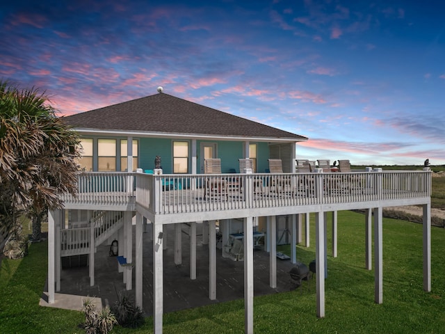 back house at dusk featuring a wooden deck and a yard