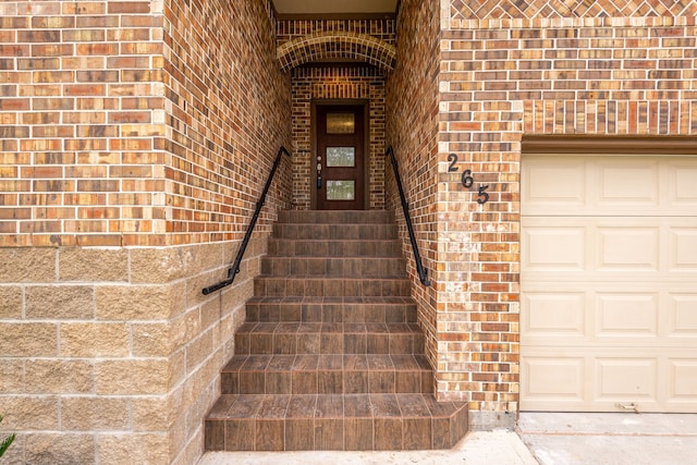 entrance to property featuring a garage and brick siding