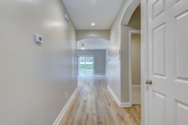 hallway featuring arched walkways, light wood-style flooring, and baseboards