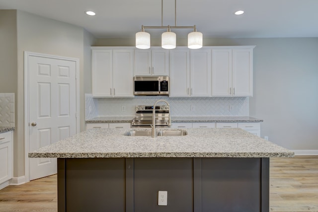 kitchen with appliances with stainless steel finishes, light wood-style floors, white cabinetry, and a sink