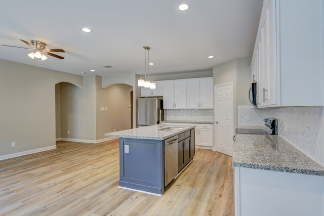 kitchen with stainless steel appliances, arched walkways, white cabinets, and light wood-style floors