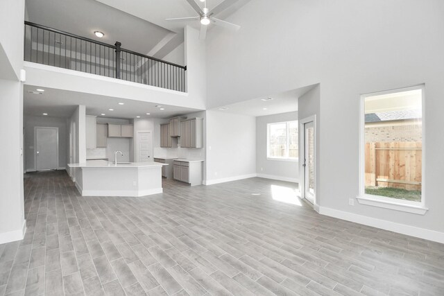 unfurnished living room with light wood-type flooring, a towering ceiling, ceiling fan, and sink