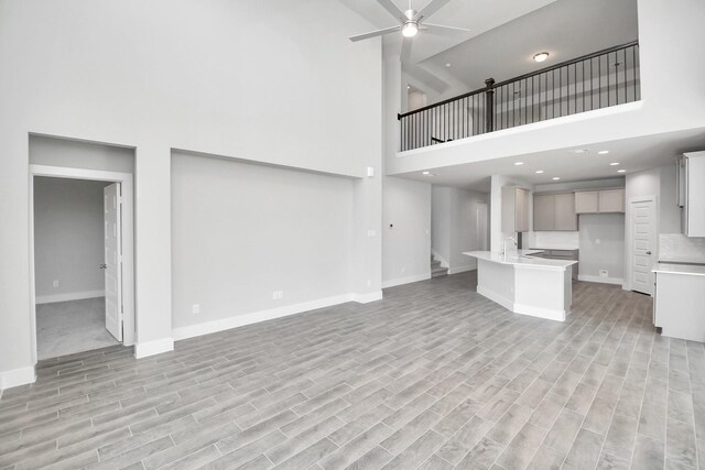 unfurnished living room featuring a high ceiling, light hardwood / wood-style floors, and ceiling fan