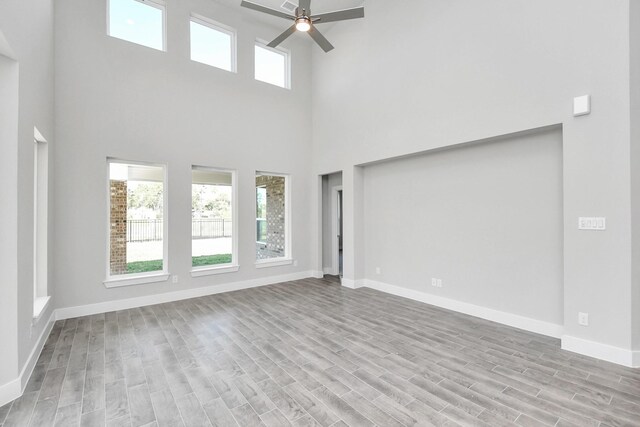 unfurnished living room with ceiling fan, light wood-type flooring, and a high ceiling