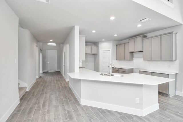 kitchen featuring kitchen peninsula, gray cabinets, light wood-type flooring, and sink