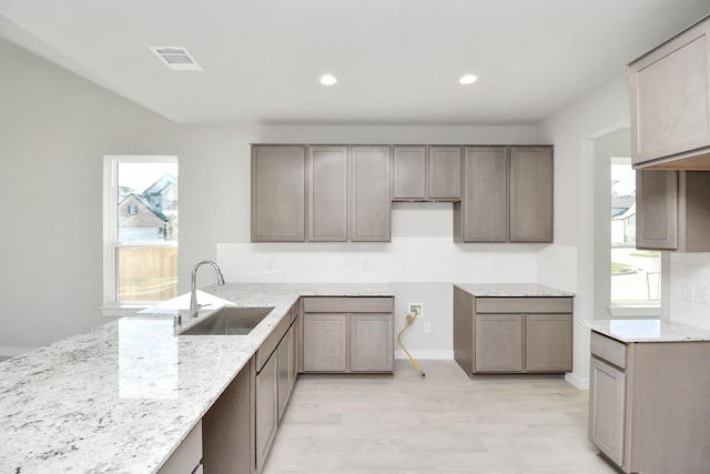 kitchen with a wealth of natural light, light stone counters, and sink