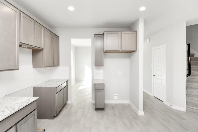 kitchen featuring gray cabinetry, light hardwood / wood-style floors, light stone counters, and tasteful backsplash