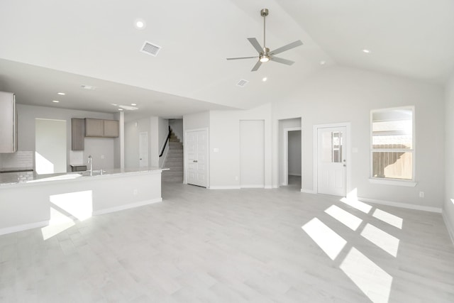 unfurnished living room with ceiling fan, sink, light hardwood / wood-style floors, and vaulted ceiling