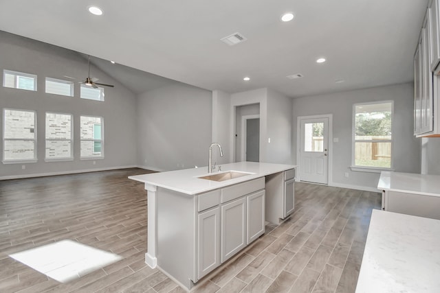 kitchen featuring sink, ceiling fan, vaulted ceiling, light hardwood / wood-style flooring, and a center island with sink