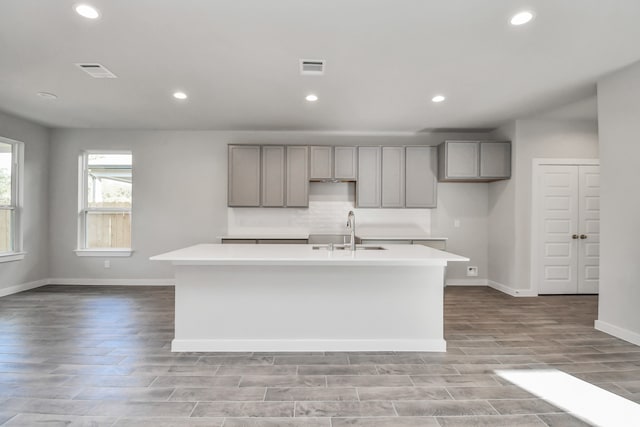 kitchen with light hardwood / wood-style floors, sink, a center island with sink, and gray cabinetry