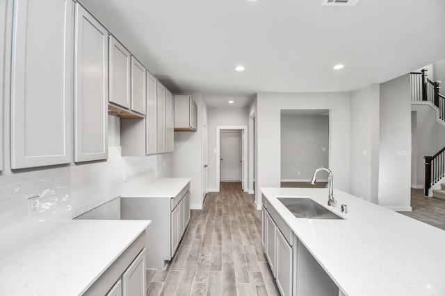 kitchen featuring light stone countertops, sink, light wood-type flooring, and gray cabinets