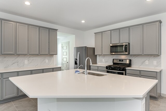 kitchen with sink, appliances with stainless steel finishes, decorative backsplash, light tile patterned floors, and a center island with sink